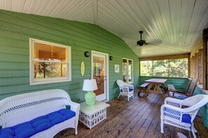 A covered porch with green walls, white wicker furniture, and a wooden table.
