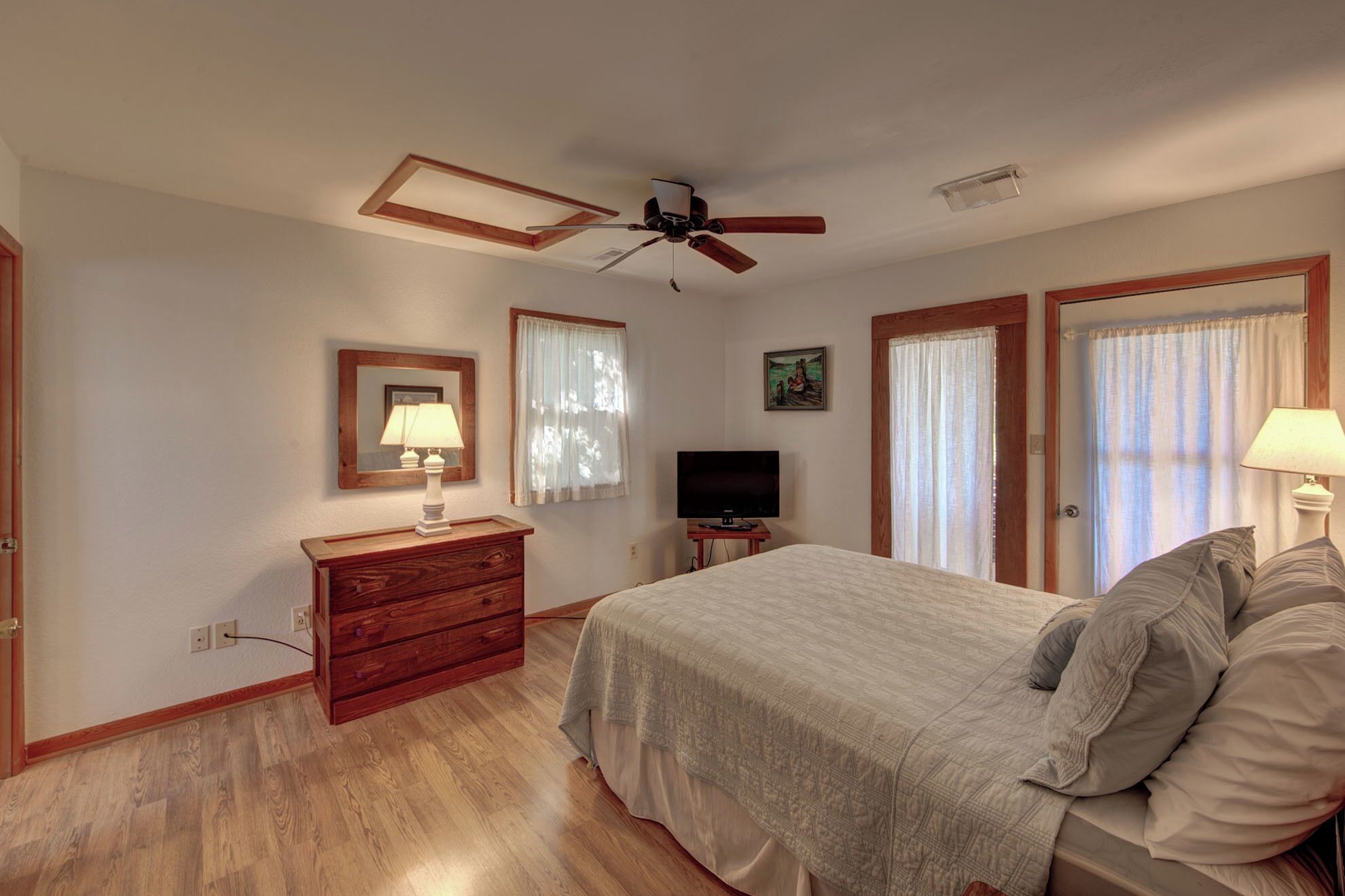 A bedroom with a bed, a dresser, a TV, and a ceiling fan.