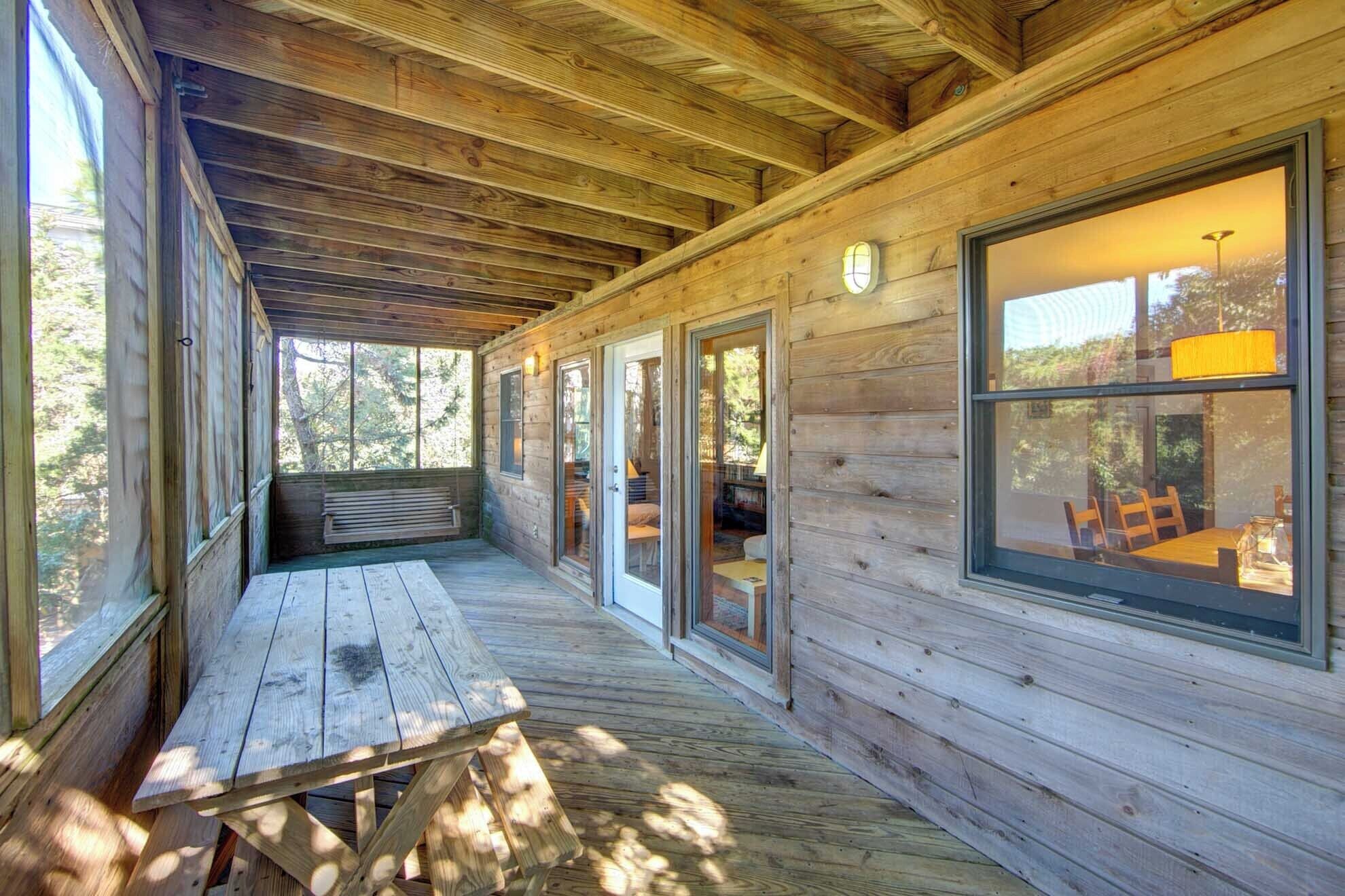 A wooden cabin with a covered porch, large windows, and a picnic table.