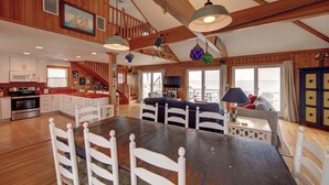A spacious kitchen with a large island, wooden beams, and a dining area with a dark table and white chairs. - Blue Oyster - Ocracoke Island (Ocracoke)