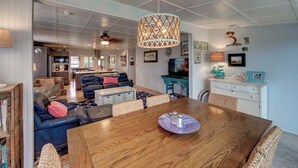 A spacious living area with a wooden dining table, blue leather sofa, and a kitchen in the background. - Fig and Thistle - Ocracoke Island (Ocracoke)