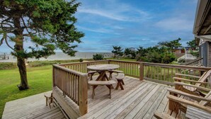 A wooden deck with a round table and benches, overlooking a beach and ocean. - Fig and Thistle - Ocracoke Island (Ocracoke)
