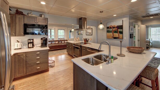 A modern kitchen with a large island, stainless steel appliances, and a view to the dining area. - Fig and Thistle - Ocracoke Island (Ocracoke)