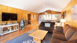 Een kamer met houten lambrisering, een bank, een bijzettafeltje, een televisie en een surfplank.