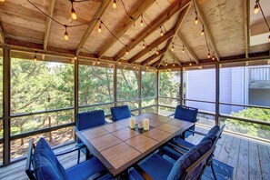 A covered outdoor dining area with a wooden table and blue chairs, surrounded by large windows offering a view of trees. - Shrimp and Grits - Ocracoke Island (Ocracoke)