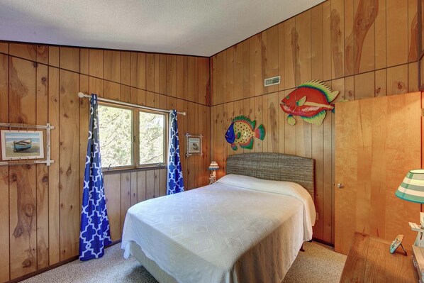 A wooden-paneled room with a bed, a window with curtains, and a fish decoration on the wall.