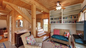 A cozy interior with a wooden ceiling, a staircase, a bookshelf, and a seating area with a television.
