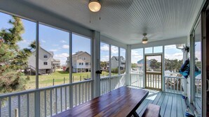 A covered outdoor area with a wooden table and benches, large windows, and a view of houses and water. - The Dory - Ocracoke Island (Ocracoke)