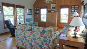 Una sala de estar acogedora con techo de madera, un sofá estampado con un motivo de peces de colores, un sillón azul y un mueble de madera.