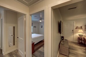 Enter a cozy bedroom with a single bed, ceiling fan, wall-mounted TV, and a small table with a lamp.