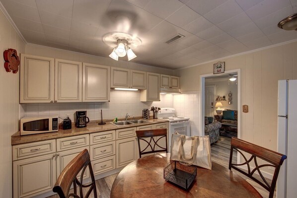Enjoy cooking and dining in this well-equipped kitchen with a central island, microwave, coffee maker, and stove, adjacent to a dining area with a round table and four chairs.