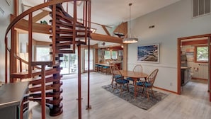 A spacious kitchen with a central island, wooden staircase, and a dining area with blue chairs.