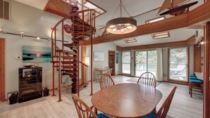 A spacious dining area with a wooden table and chairs, a spiral staircase, and large windows offering views of the outdoors.