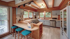 A kitchen with wooden beams, a central island with stools, and large windows.