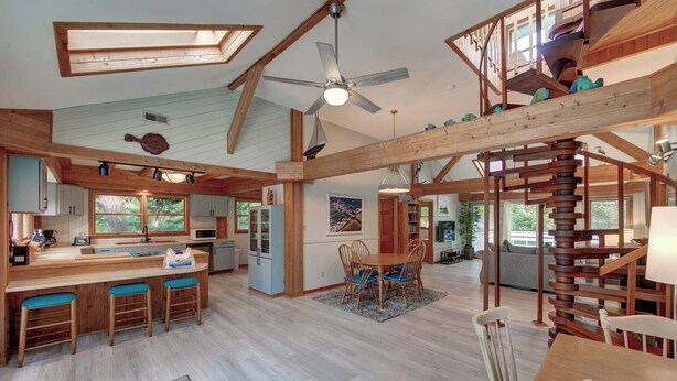 A spacious loft-style interior with a high ceiling, exposed wooden beams, a central dining area, and a kitchen with a large island.