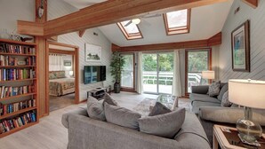 A spacious living room with a high ceiling, wooden beams, a large sofa, a television, and a bookshelf filled with books.