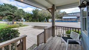 Une véranda couverte avec une balustrade en bois, un banc et une vue sur une rue bordée d’arbres, avec un bâtiment en arrière-plan.