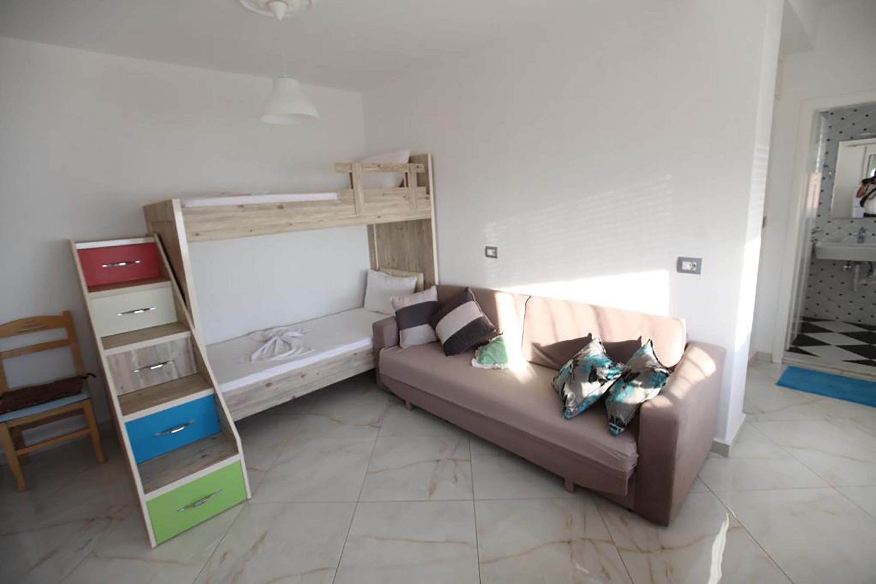 Una habitación con una cama nido, un sofá, una silla y un escritorio con cajones.