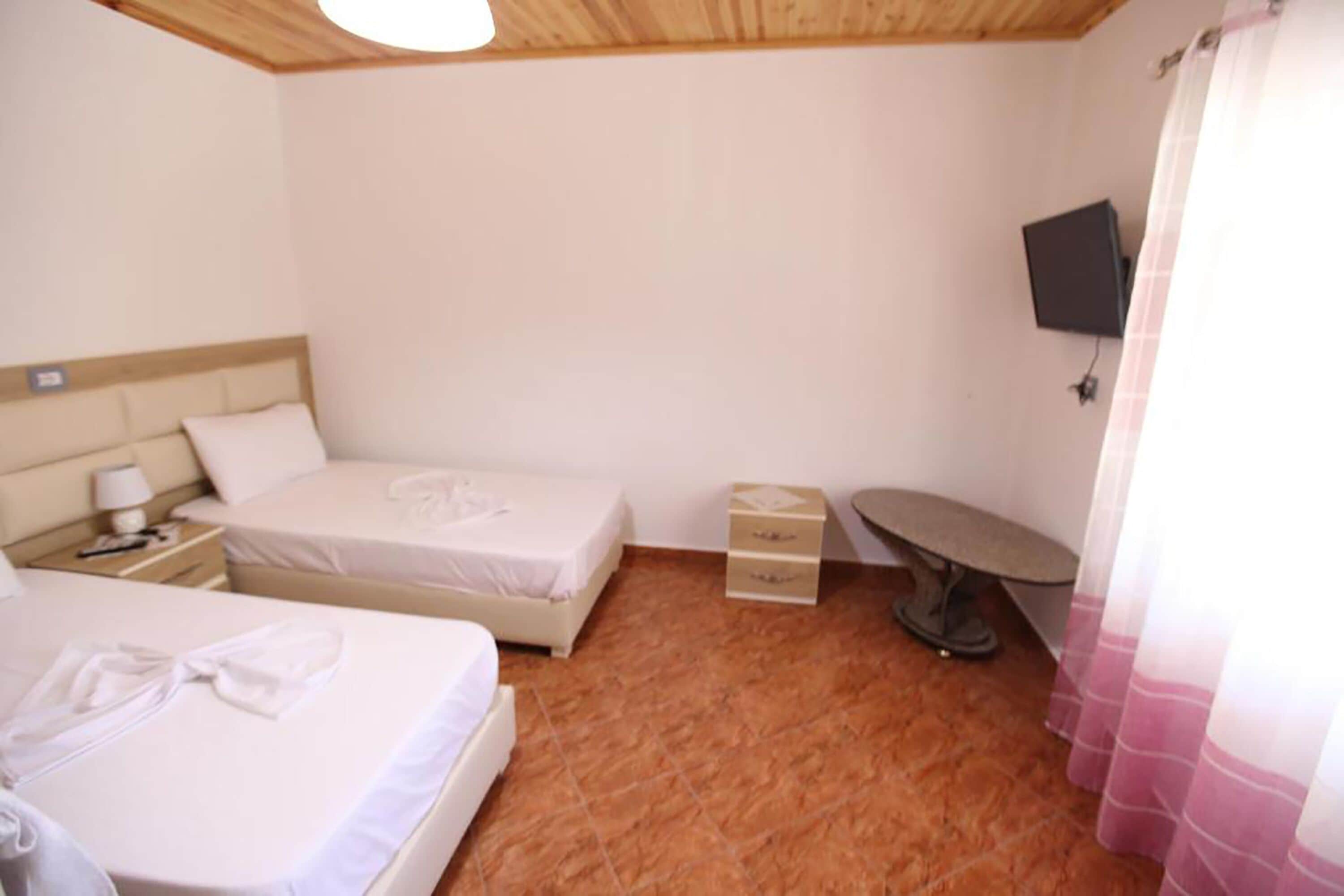 Une chambre d’hôtel avec deux lits, une télévision, un petit bureau et un porte-chaussures.
