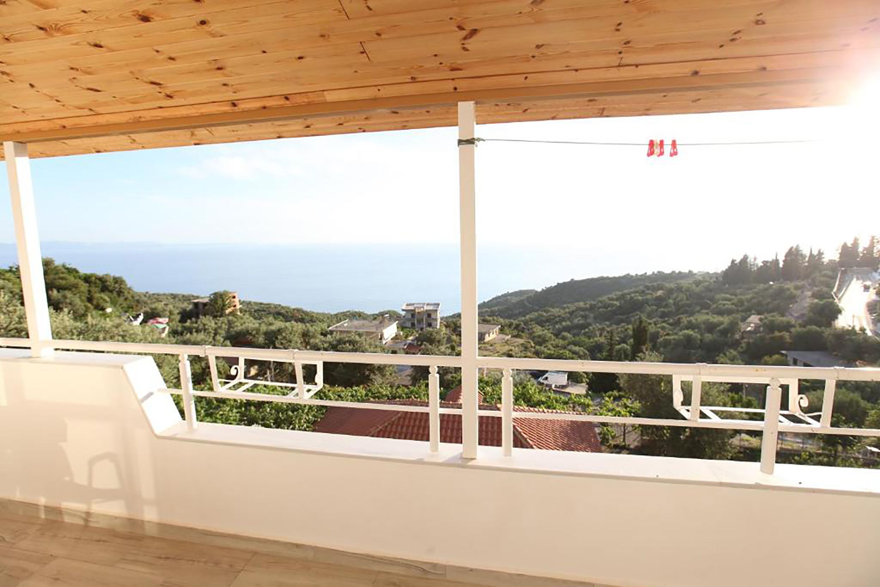 A balcony with a wooden ceiling overlooking a scenic landscape with houses and greenery.