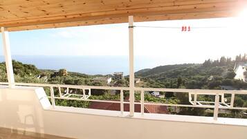 A balcony with a wooden ceiling overlooking a scenic landscape with houses and greenery.