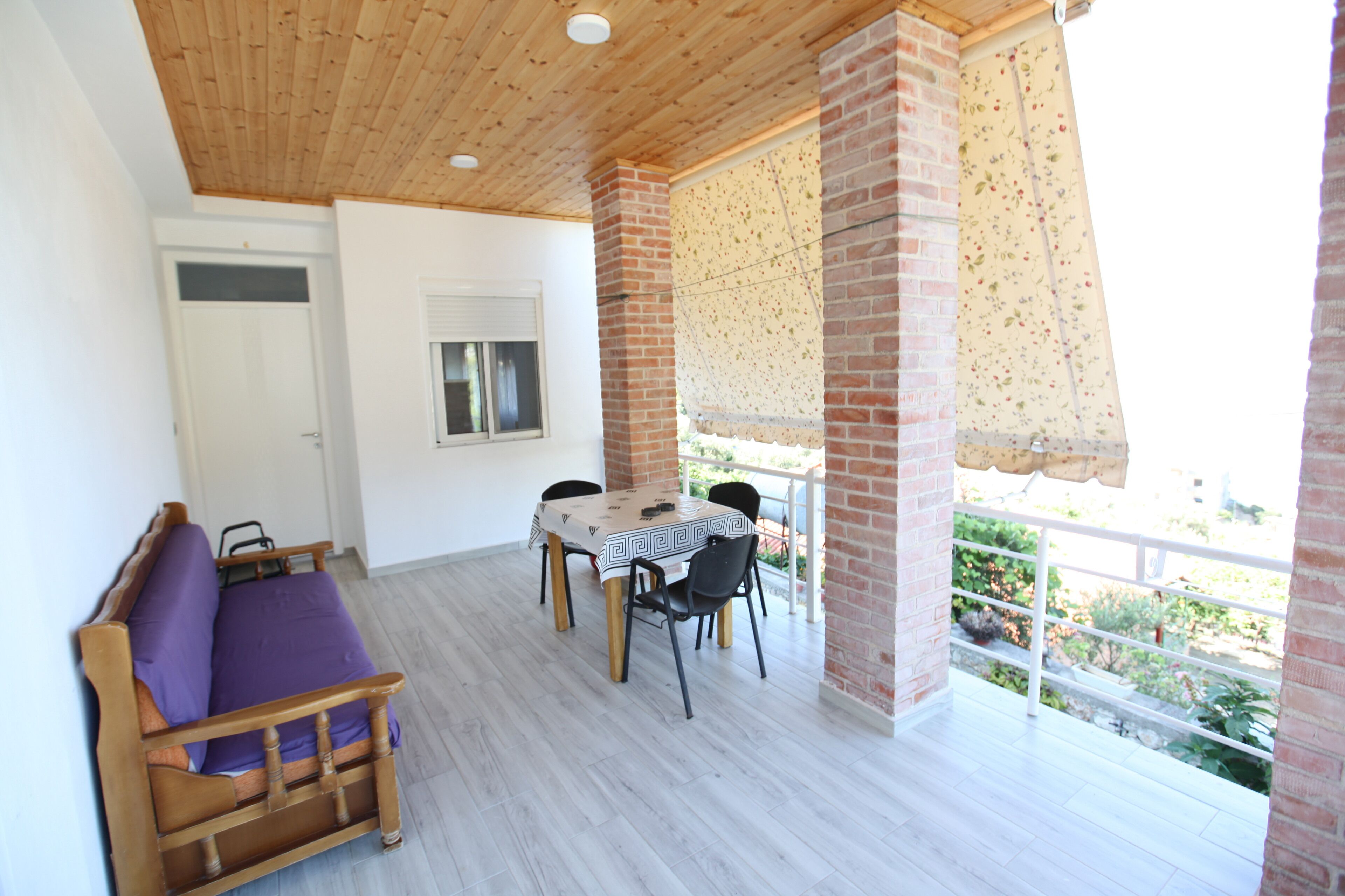 Una habitación con techo de madera, una mesa de comedor con sillas, un sofá morado y un ventanal con vistas a un jardín.