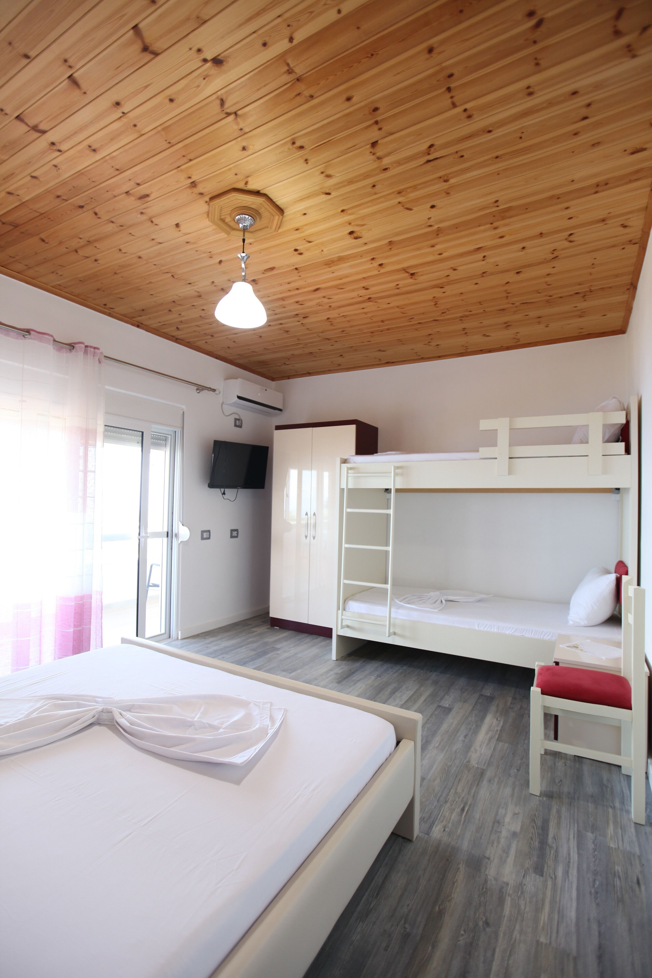 A room with a bunk bed, a single bed, a TV mounted on the wall, and a wooden ceiling.