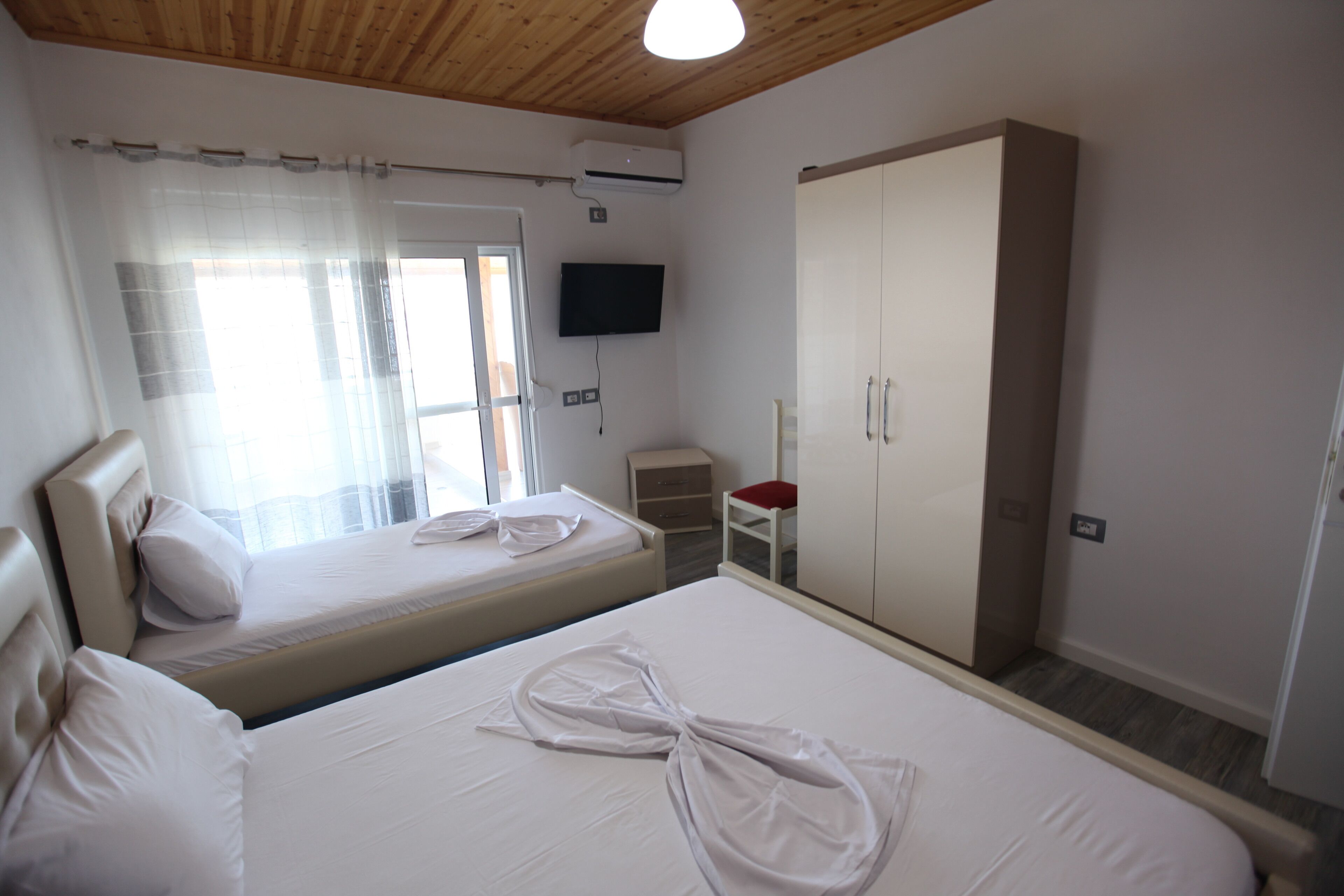 A hotel room with two beds, a TV, a wardrobe, and a small table.