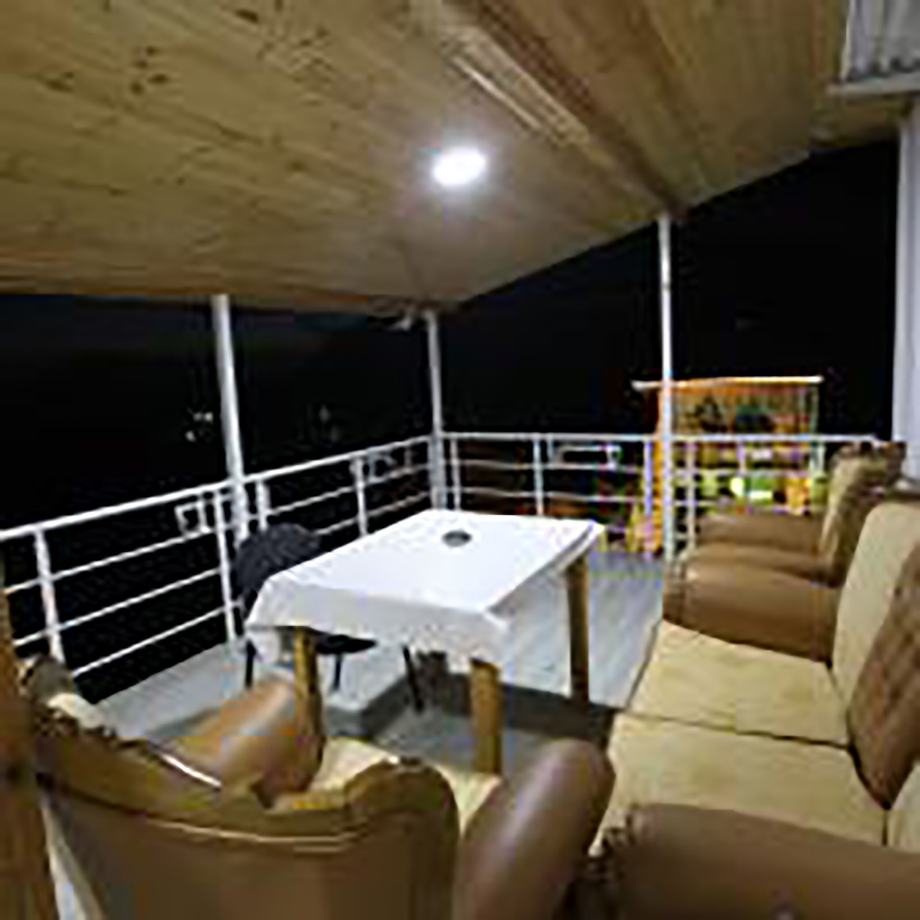 Un patio al aire libre con una mesa, sillas, barandilla y vista al cielo nocturno.