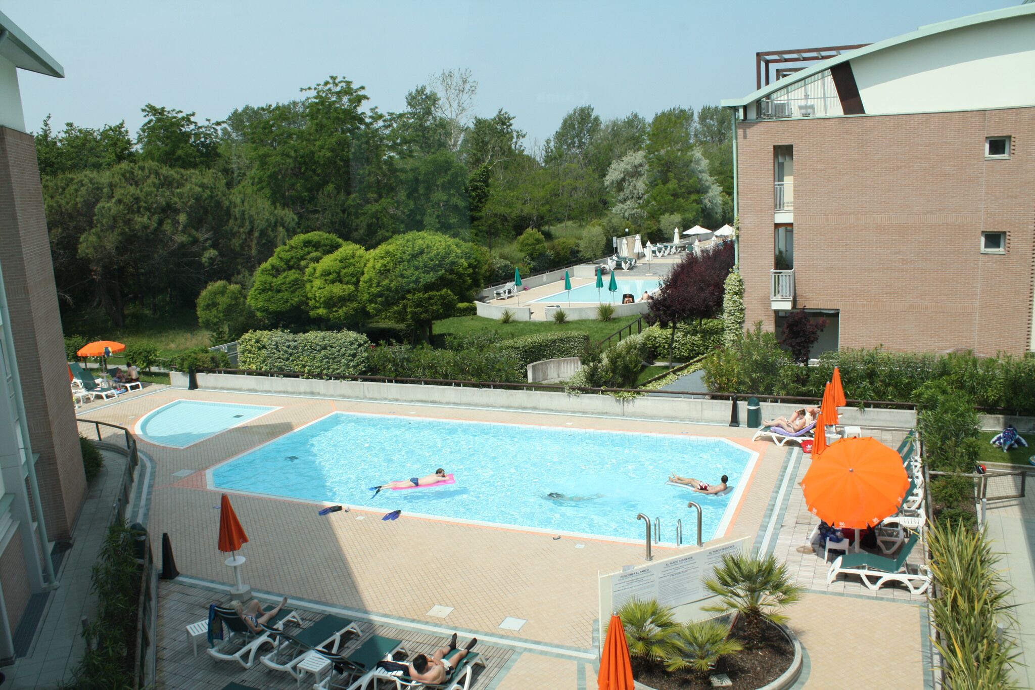 A rooftop swimming pool with multiple lanes, surrounded by lounge chairs and umbrellas, and a view of a forested area.