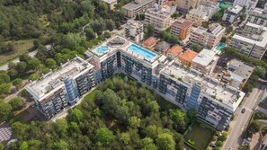 Un immeuble résidentiel de grande hauteur doté de nombreux balcons, d’une piscine sur le toit et entouré de verdure.