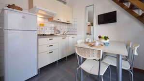 A modern kitchen with white cabinets, a built-in stove, and a dining area with a white table and chairs. - Holiday apartment with air conditioning and balcony (Bibione)