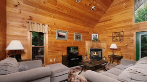 A cozy log cabin interior with a fireplace, two sofas, a TV, and framed pictures on the walls. - Hidden Ecstasy: Your Secret Mountain Bliss (Sevierville)