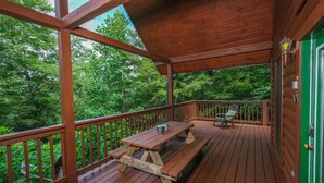 A wooden deck with a picnic table and chairs, surrounded by lush greenery. - Hidden Ecstasy: Your Secret Mountain Bliss (Sevierville)