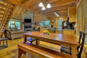 A cozy cabin interior with a wooden dining table, benches, a fireplace, a kitchen area, and a stone accent wall. - Pet-friendly lakeside retreat with fire pit, hot tub, pool table, canoe, fishing dock, and WiFi for ultimate relaxation-LVE (Ellijay)