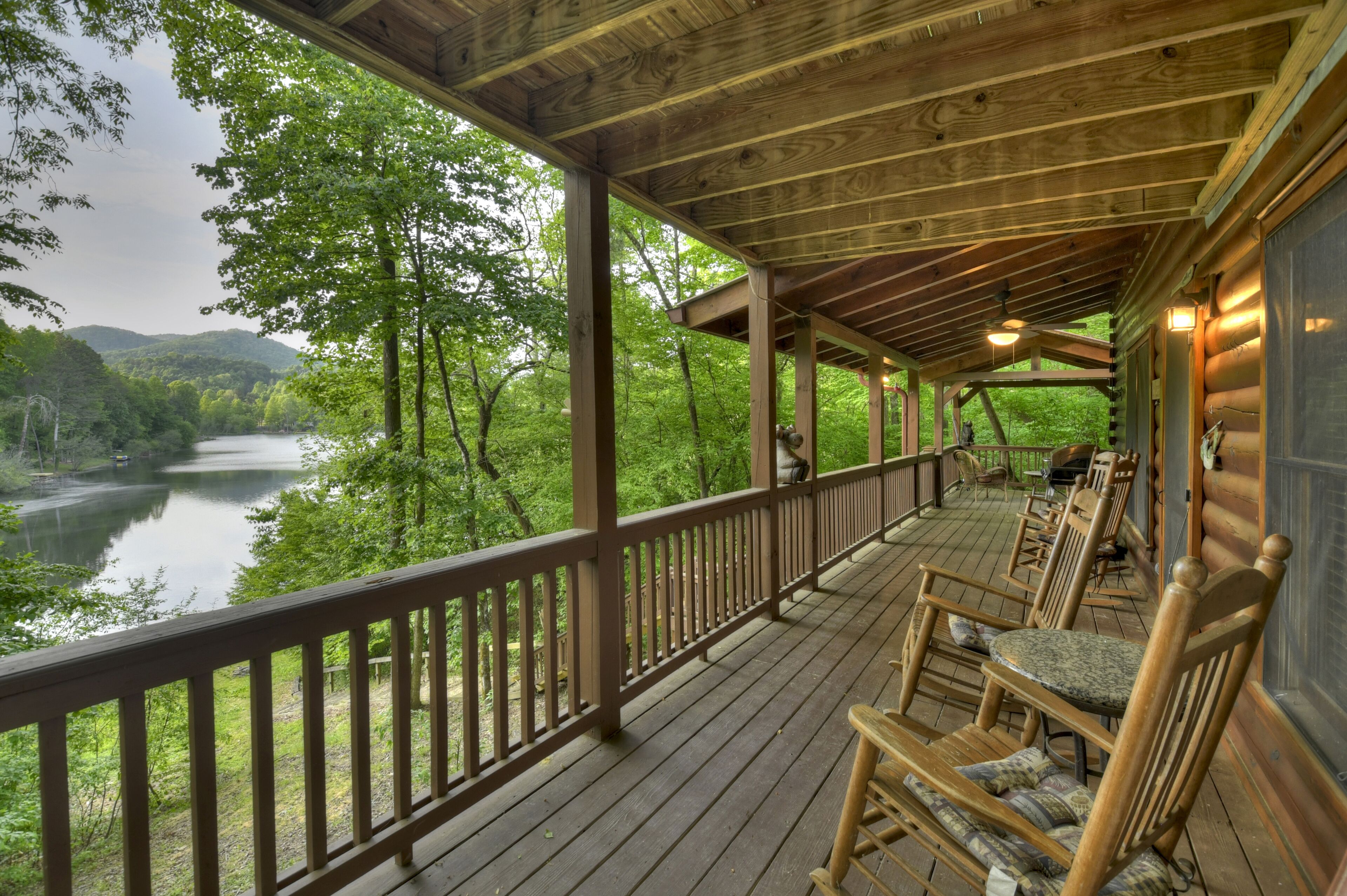 A wooden deck with chairs overlooking a lake surrounded by trees.