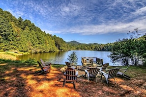 Un entorno junto al lago con sillas Adirondack y una terraza de madera con vistas a un lago, rodeado de colinas boscosas.