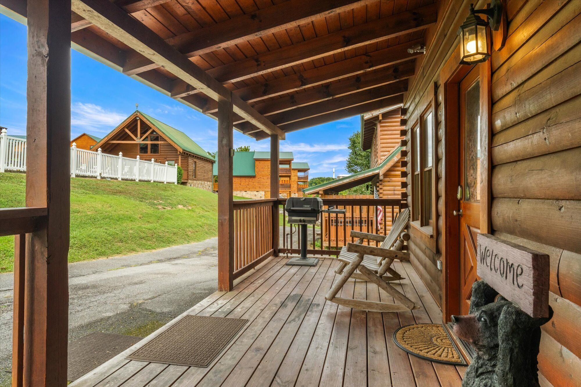 A wooden cabin with a porch, a welcome sign, and a barbecue grill.