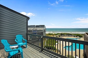 Un balcon avec vue sur l’océan, une piscine et une terrasse aménagée avec des chaises.