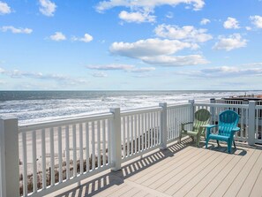 A wooden deck with a white railing overlooking the ocean.
