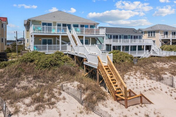 A beachfront property with multiple levels, wooden staircases, and a sandy beach area.