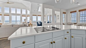 A spacious kitchen with a large island, white cabinetry, and gold handles. There are multiple windows providing views of the ocean. - New River Inlet Rd. 650 (North Topsail Beach)