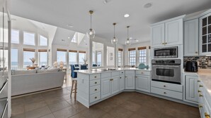 A modern kitchen with white cabinetry, a central island, and a dining area with a view. - New River Inlet Rd. 650 (North Topsail Beach)