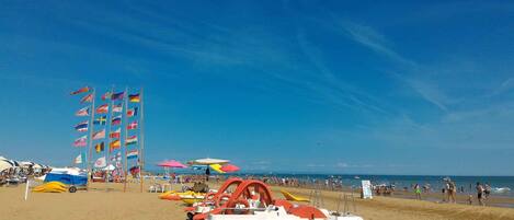 Una playa con banderas, sombrillas y barcos.