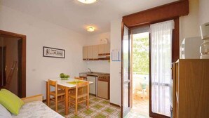 A compact room with a bed, a small dining table, a kitchenette, and a sliding glass door leading to an outdoor area. - Holiday apartment with balcony and air conditioning (Bibione)