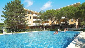 A swimming pool surrounded by trees and a building with balconies. - Holiday apartment with balcony and air conditioning (Bibione)