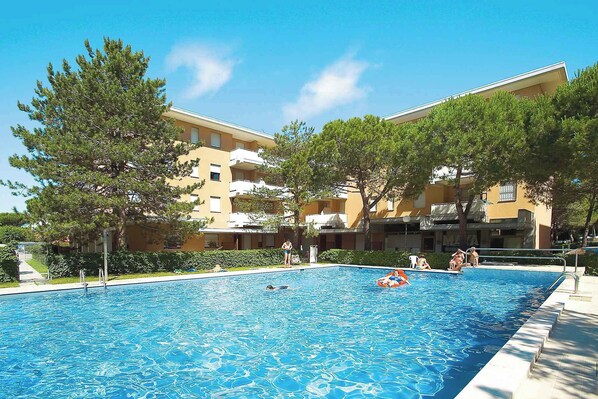 A swimming pool surrounded by trees and a building with balconies.