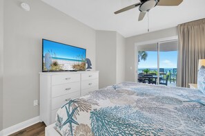 Une chambre à coucher avec un lit, un téléviseur posé sur une commode, un ventilateur de plafond et un balcon avec vue.