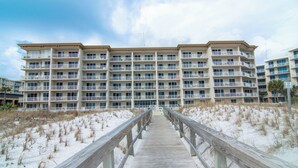 A multi-story hotel with a wooden boardwalk leading to the entrance, surrounded by sand dunes.