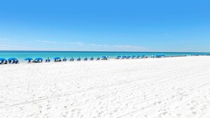 A wide sandy beach with blue umbrellas and lounge chairs.